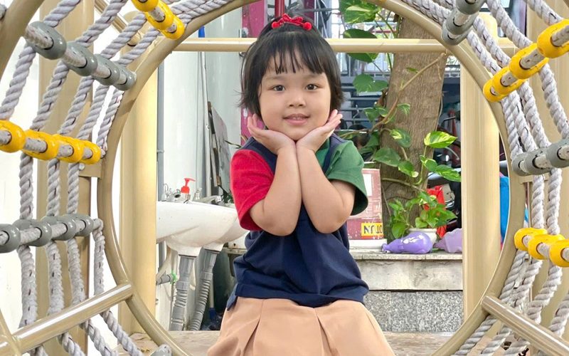 Bé gái mặc đồng phục cười trong khu leo trèo