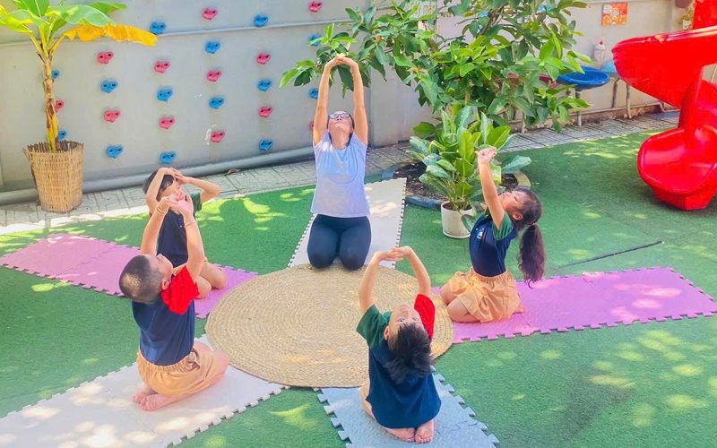 Cô và các bé tập vươn người trên thảm ngoài sân